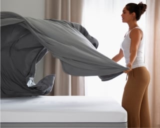 A woman fanning out sheets over a bed.