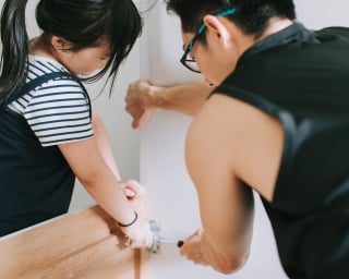 An adult and a child adjust the joints on a squeaky bed frame.
