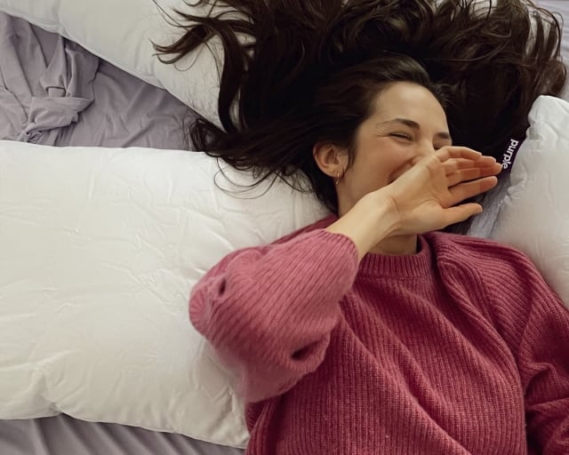 Woman lying on her back surrounded by three Purple pillows. 