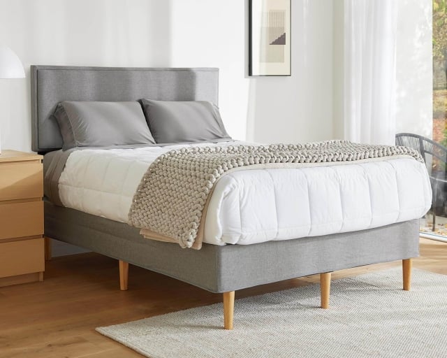 A mattress covered with a duvet and blanket on top of the Purple Bed Frame in a bright bedroom.