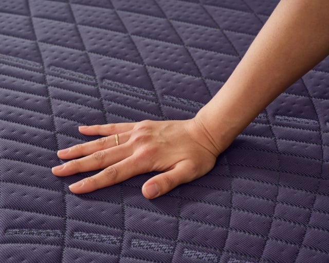 A hand pressing into the top of a new Rejuvenate mattress from Purple.