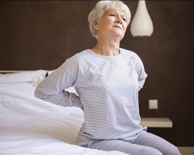 An older woman waking up with back pain.