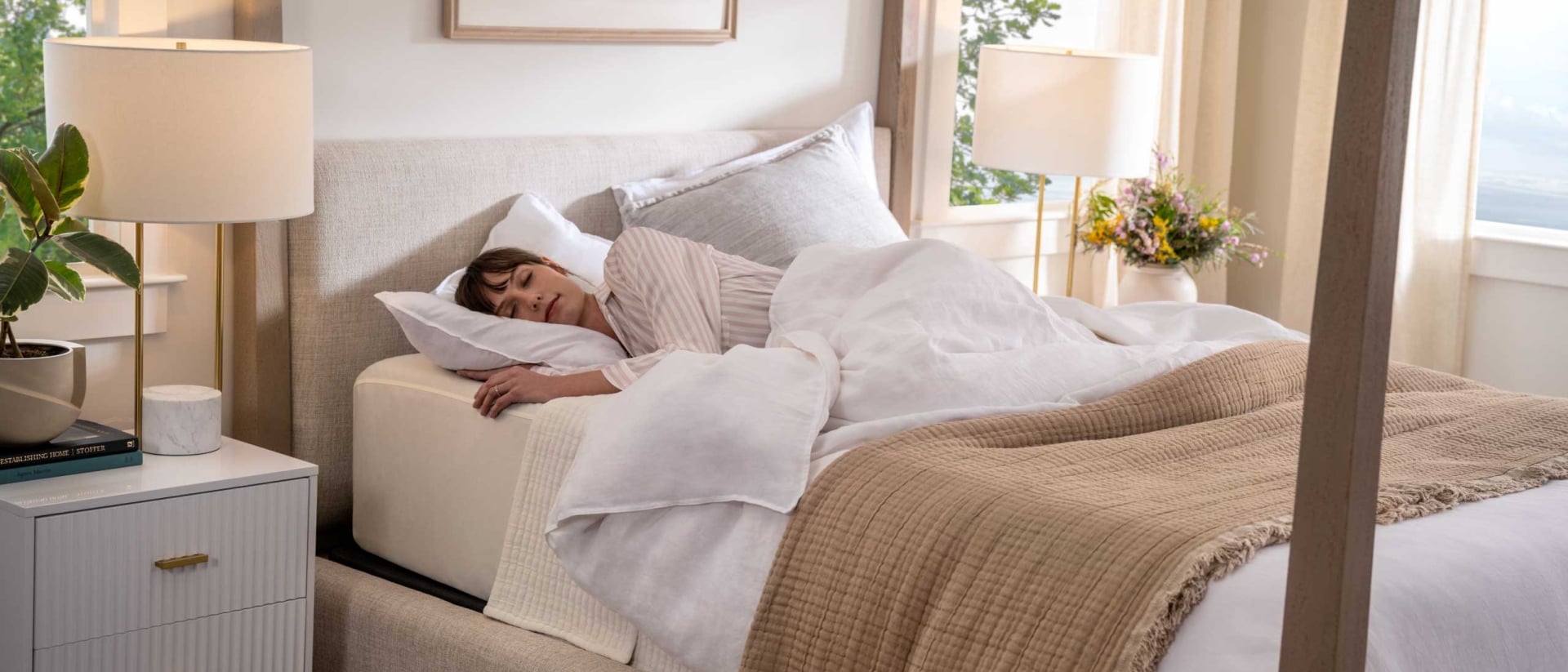 A woman sleeping on her side in a brightly lit room on a cozy bed