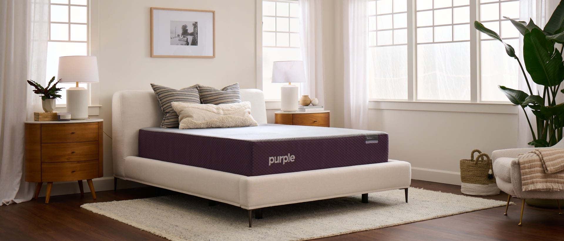 A queen Purple mattress on a cream bed frame in a bright airy bedroom.